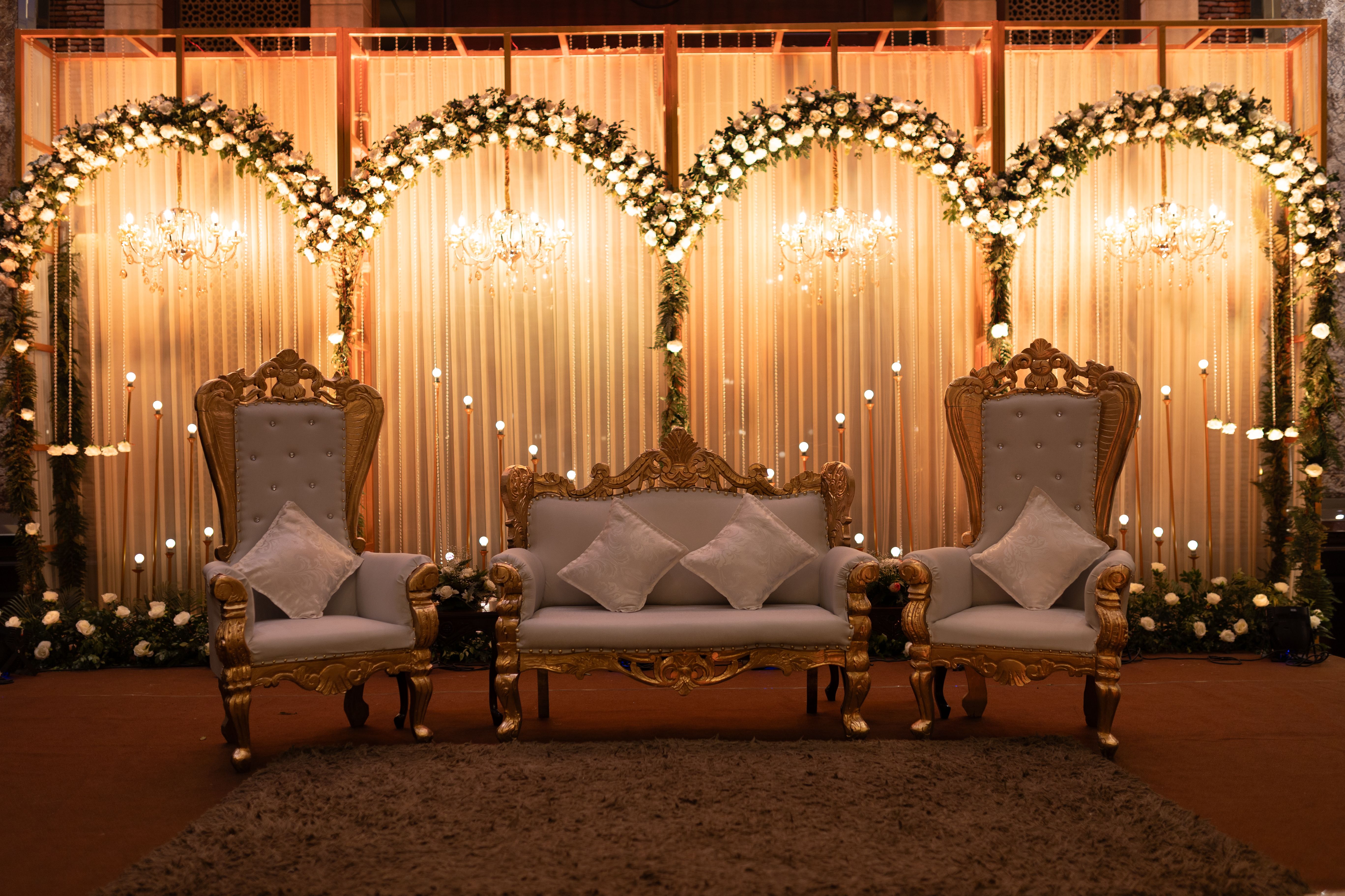 Elegant wedding stage set with ornate chairs and floral decorations under warm lighting.