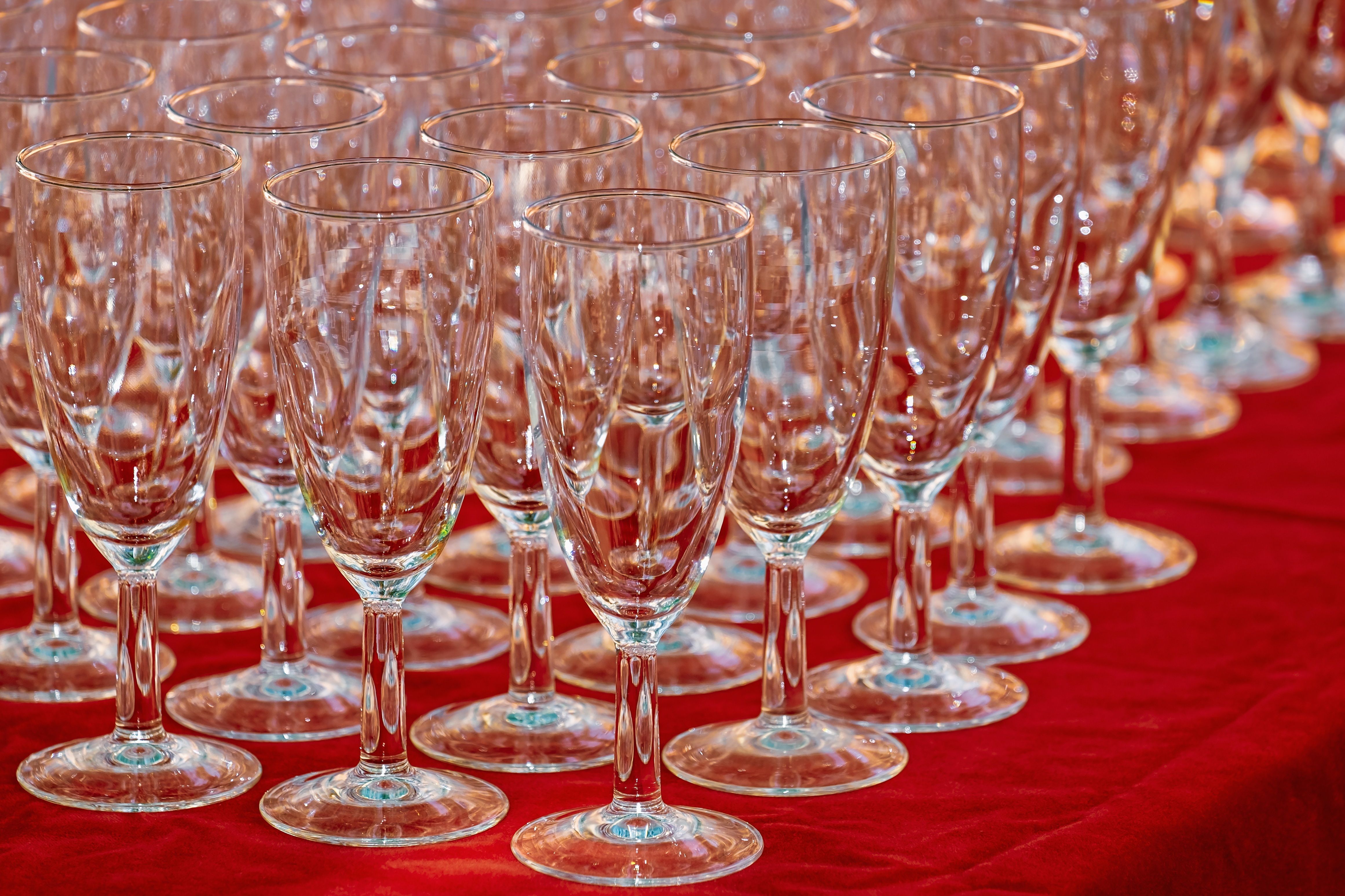 Rows of empty crystal glasses on a vibrant red tablecloth, ready for an event.