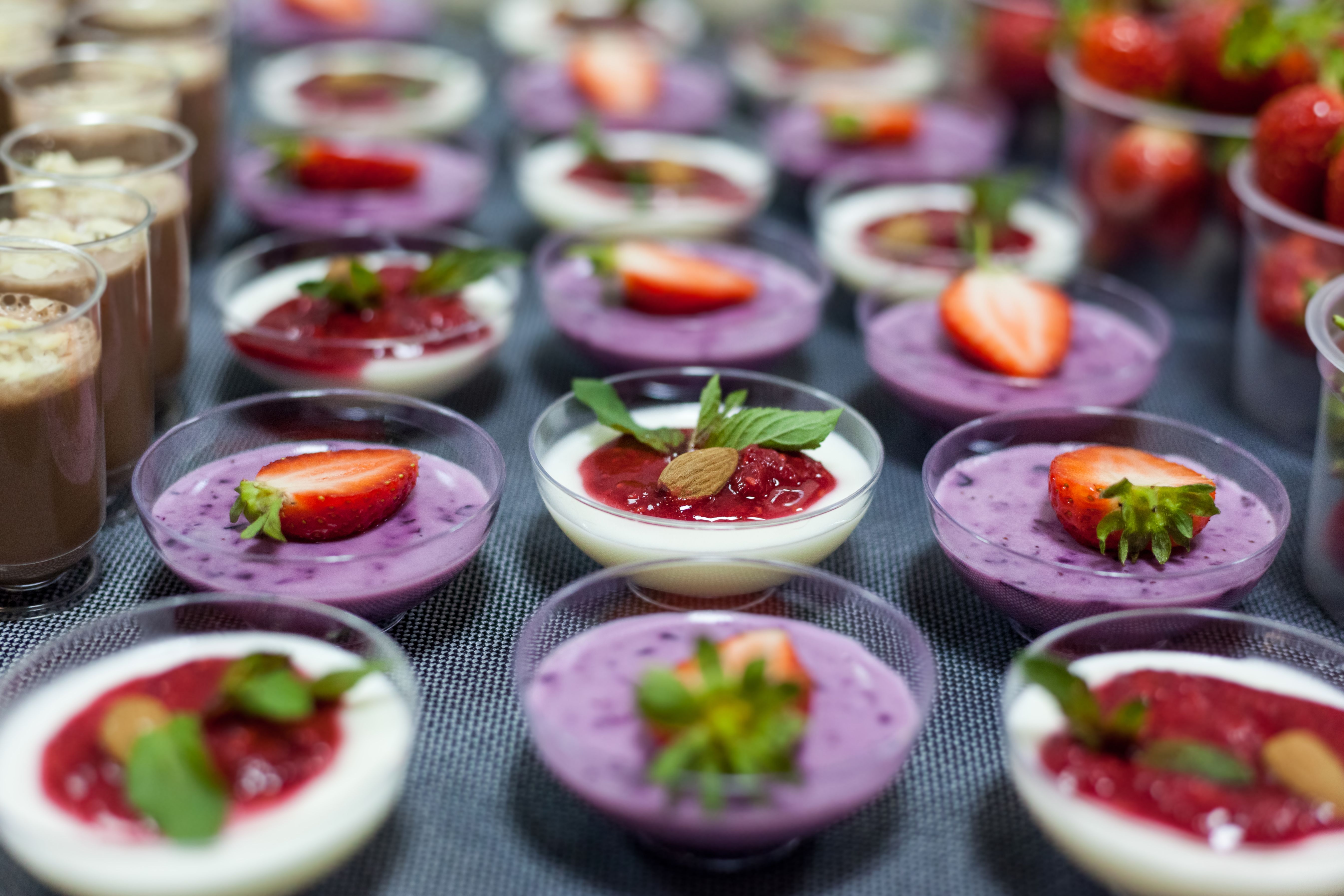 A variety of panna cotta desserts topped with fresh strawberries and mint leaves, creating a vibrant and sweet presentation.