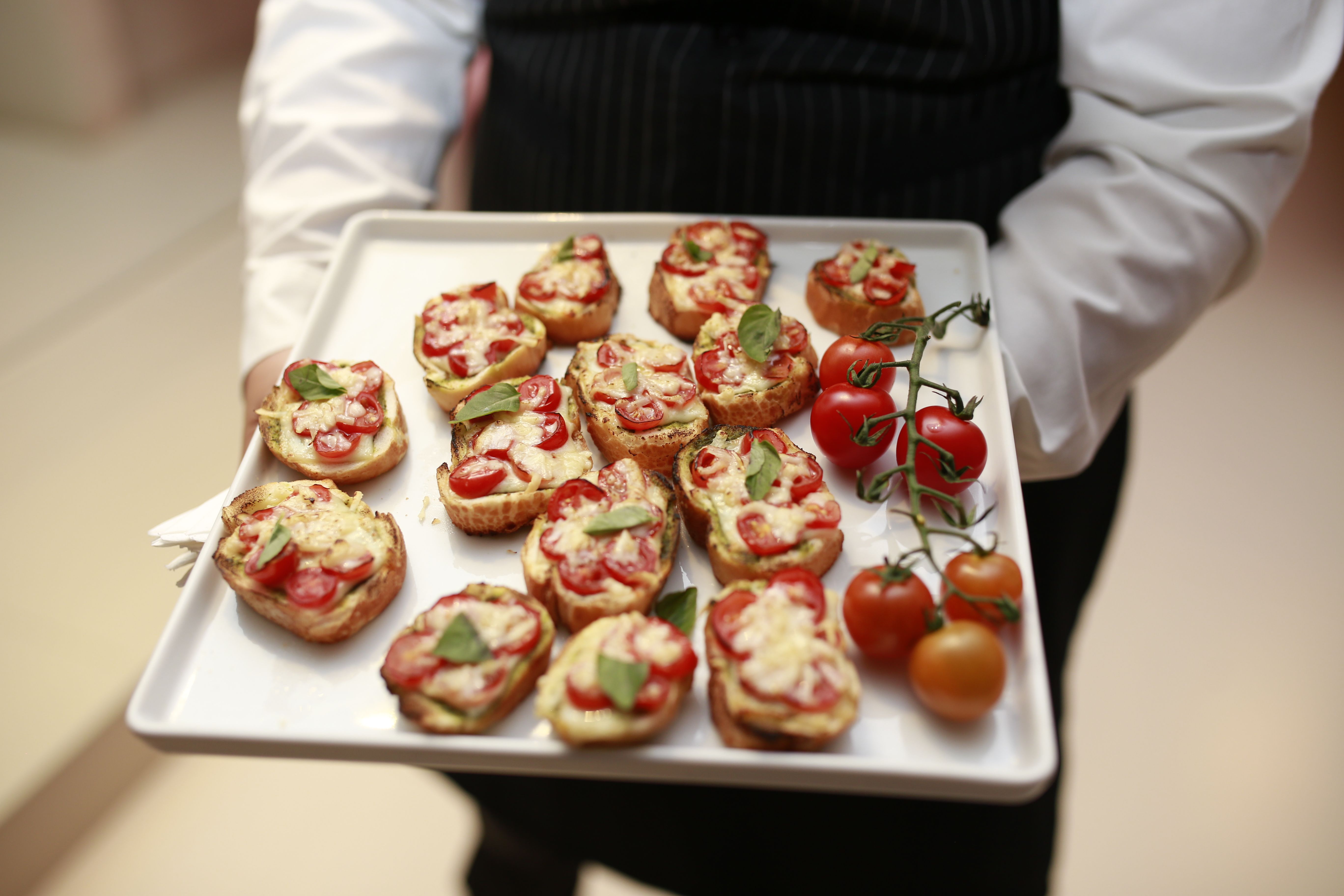 A waiter presents a tray of gourmet bruschetta with fresh tomatoes and basil.