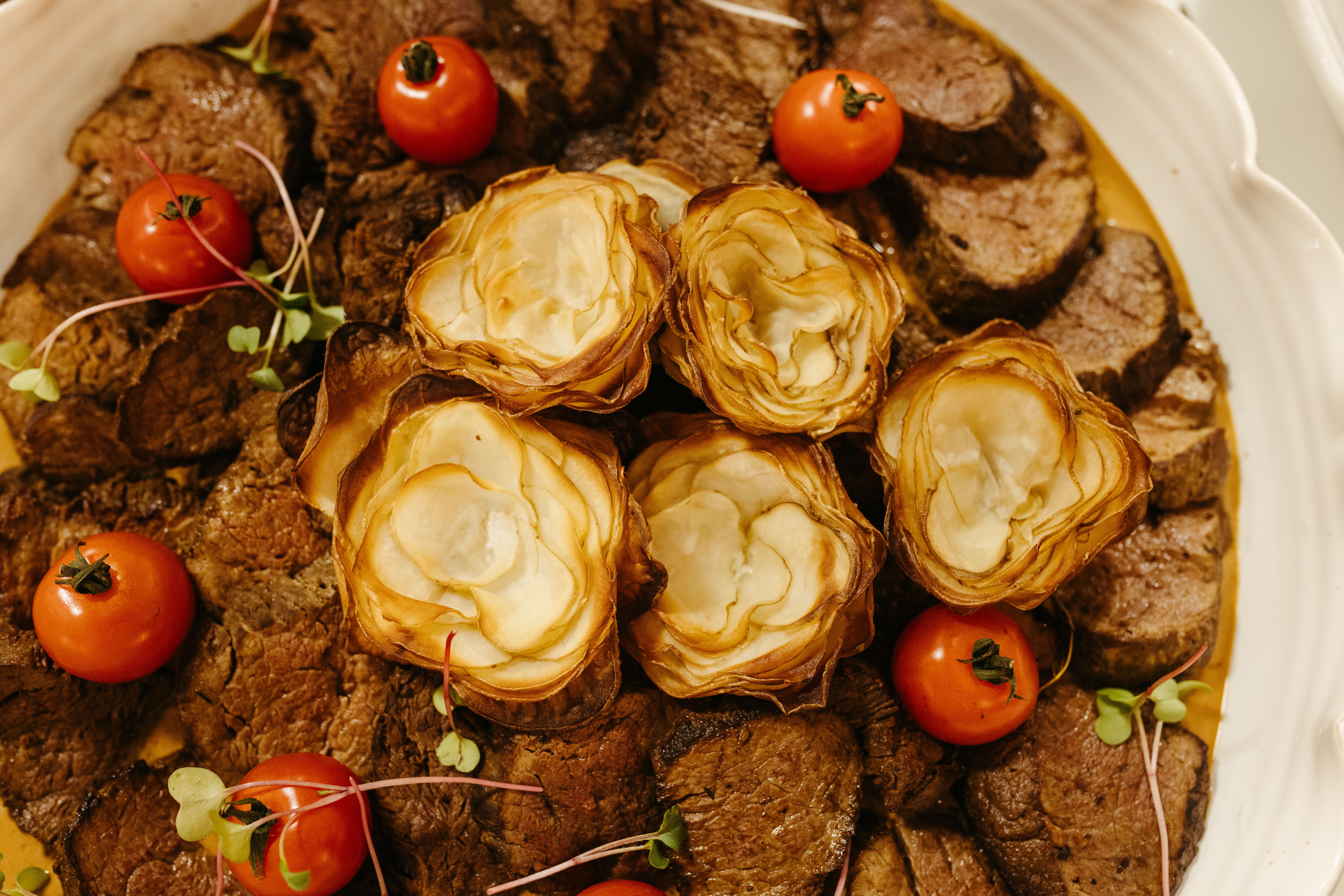 A delectable gourmet dish featuring roasted meats, crispy potatoes, and fresh cherry tomatoes.