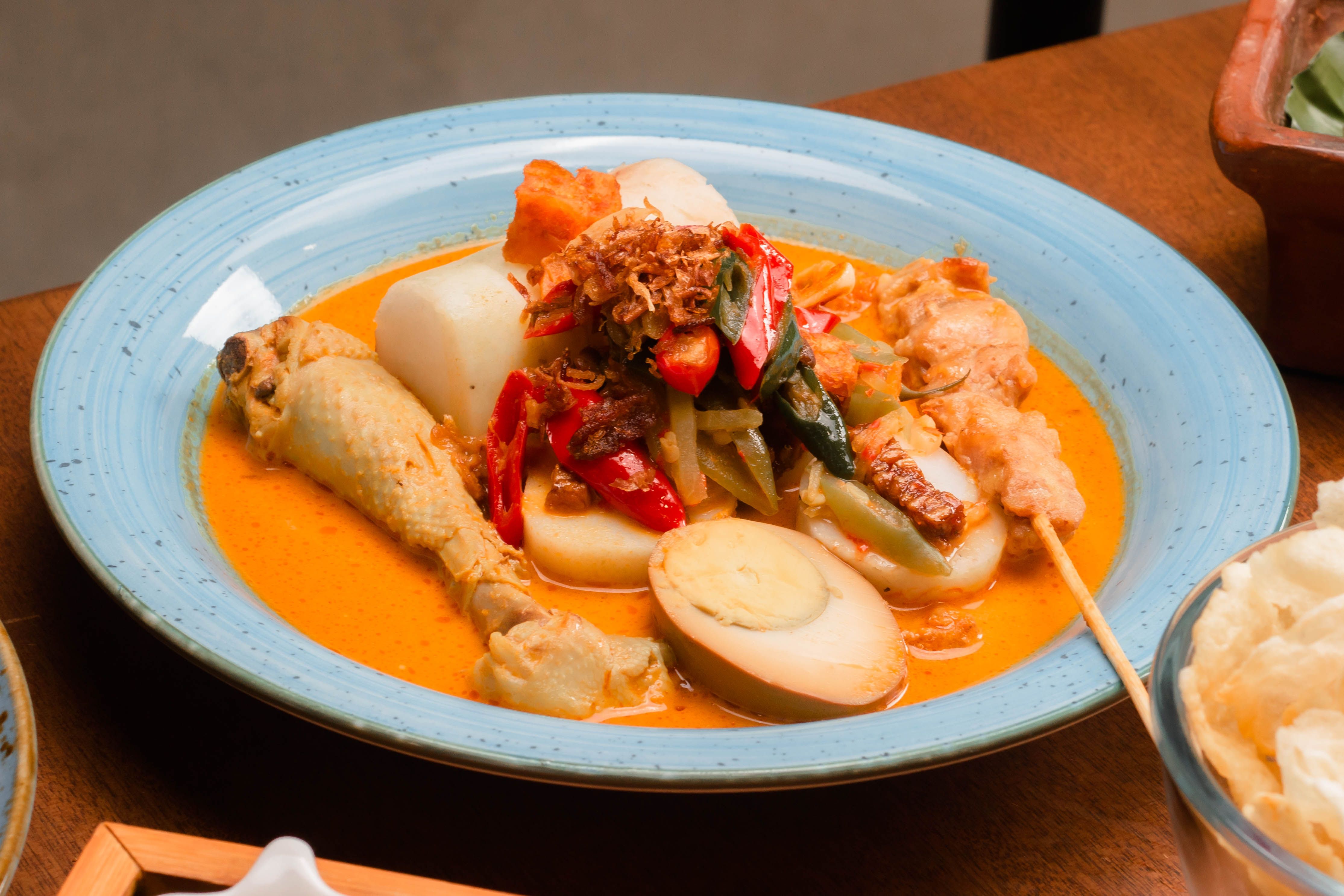 A vibrant plate of Indonesian lontong sayur with chicken, vegetables, and spicy coconut gravy.