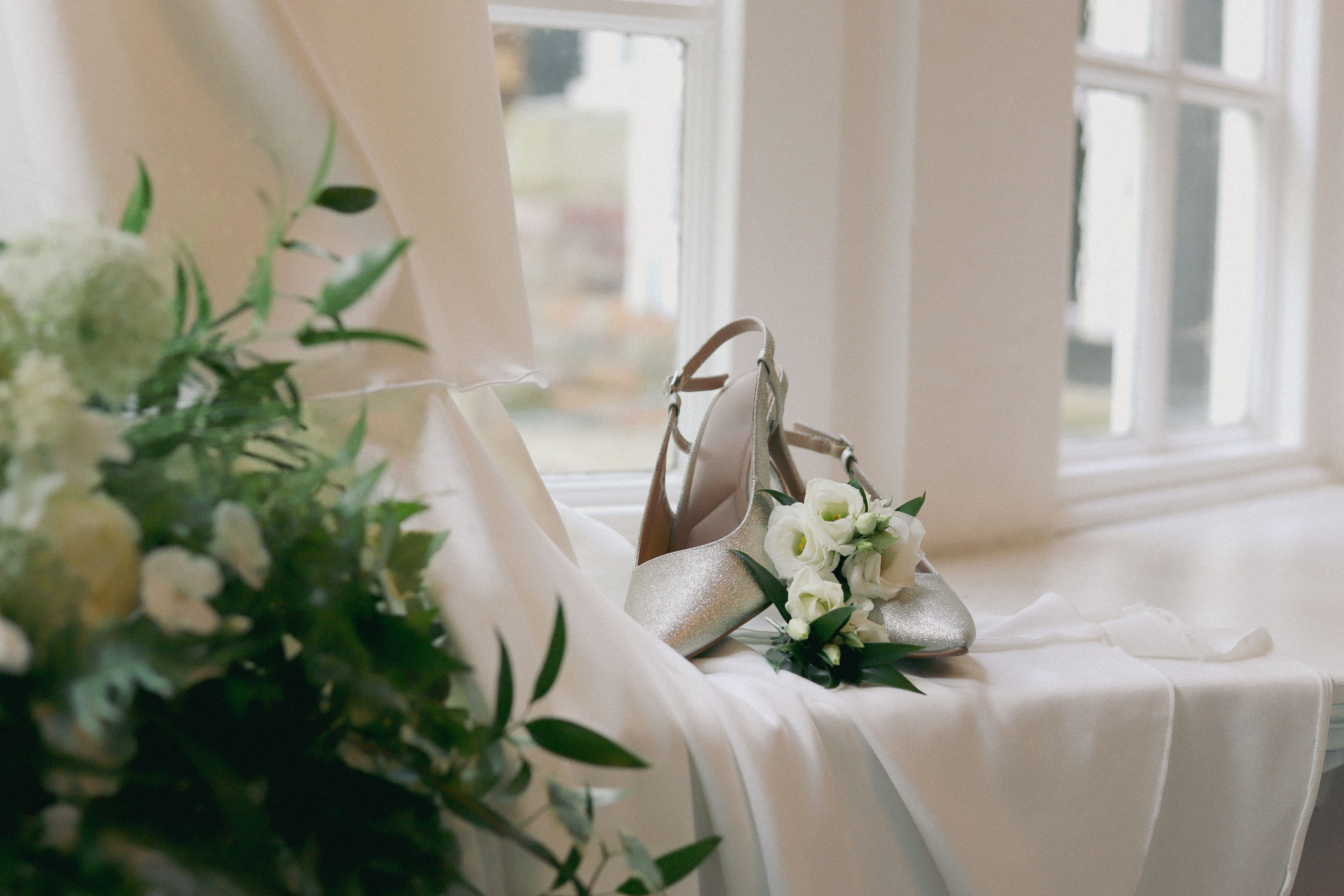 Beautiful bridal shoes and floral bouquet arranged by a wedding dress, capturing the elegance of a wedding day.