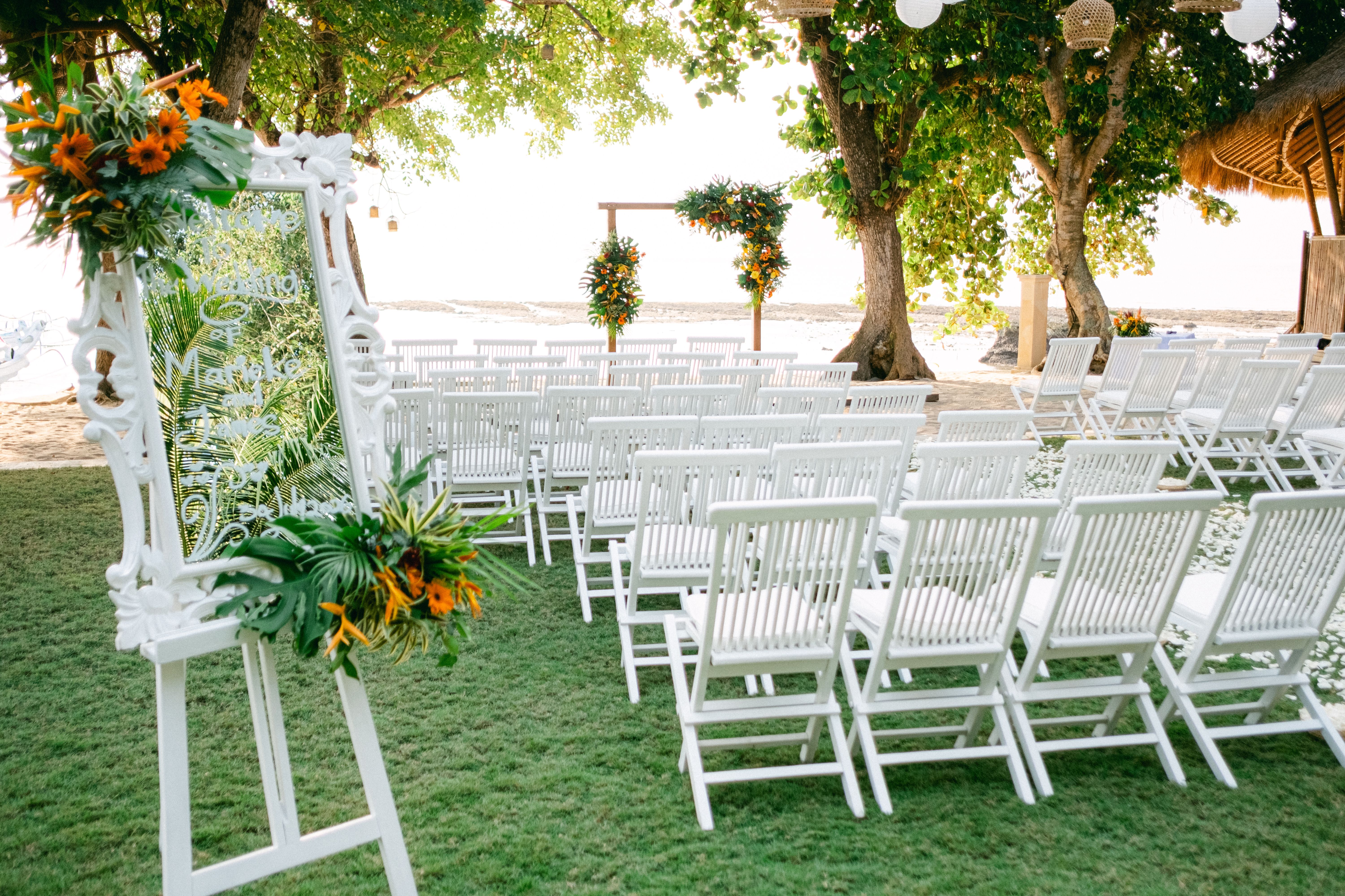 Elegant outdoor wedding setup with white chairs and floral arrangements near a beach.