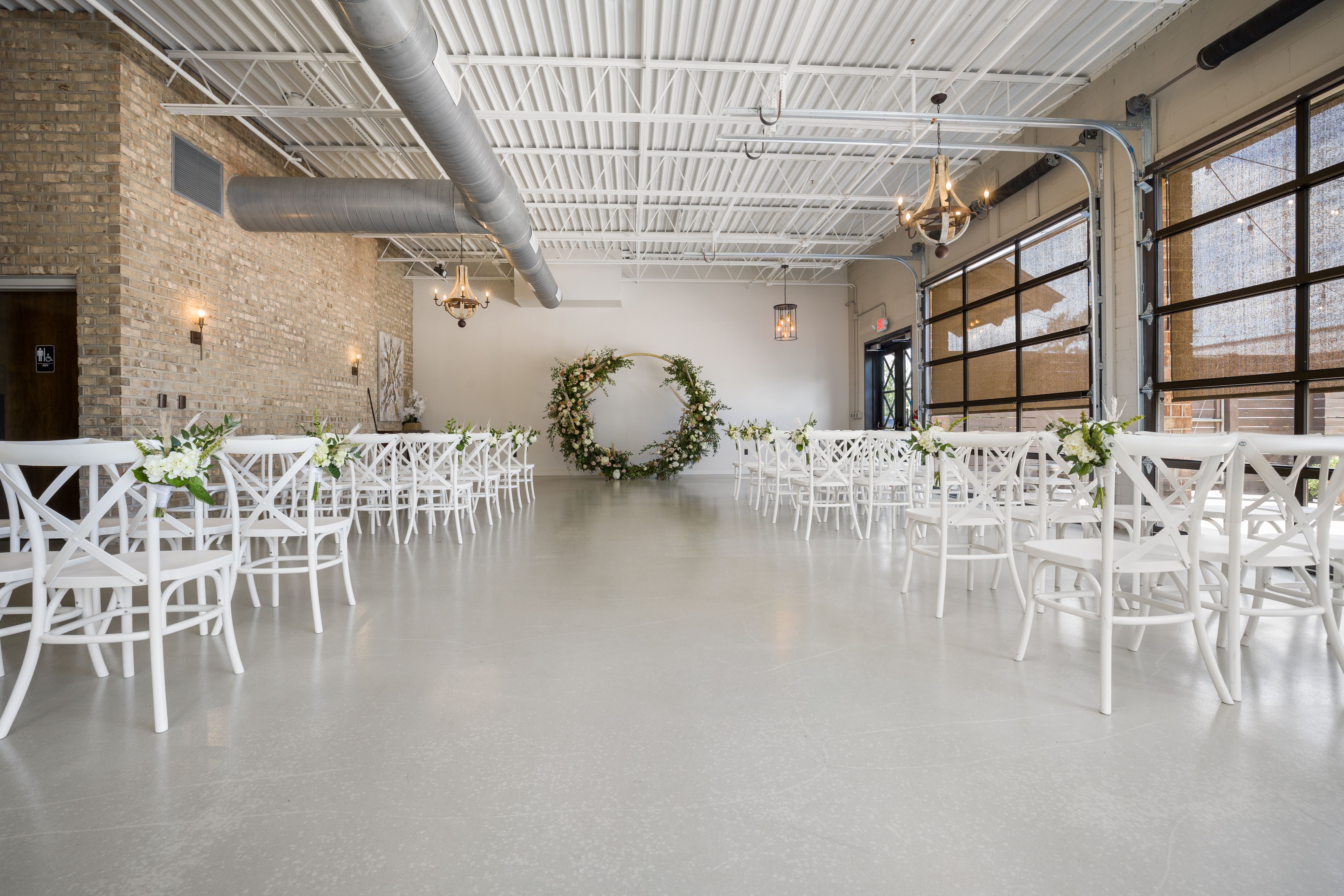 Spacious indoor wedding reception venue with elegant floral decorations and white chairs.
