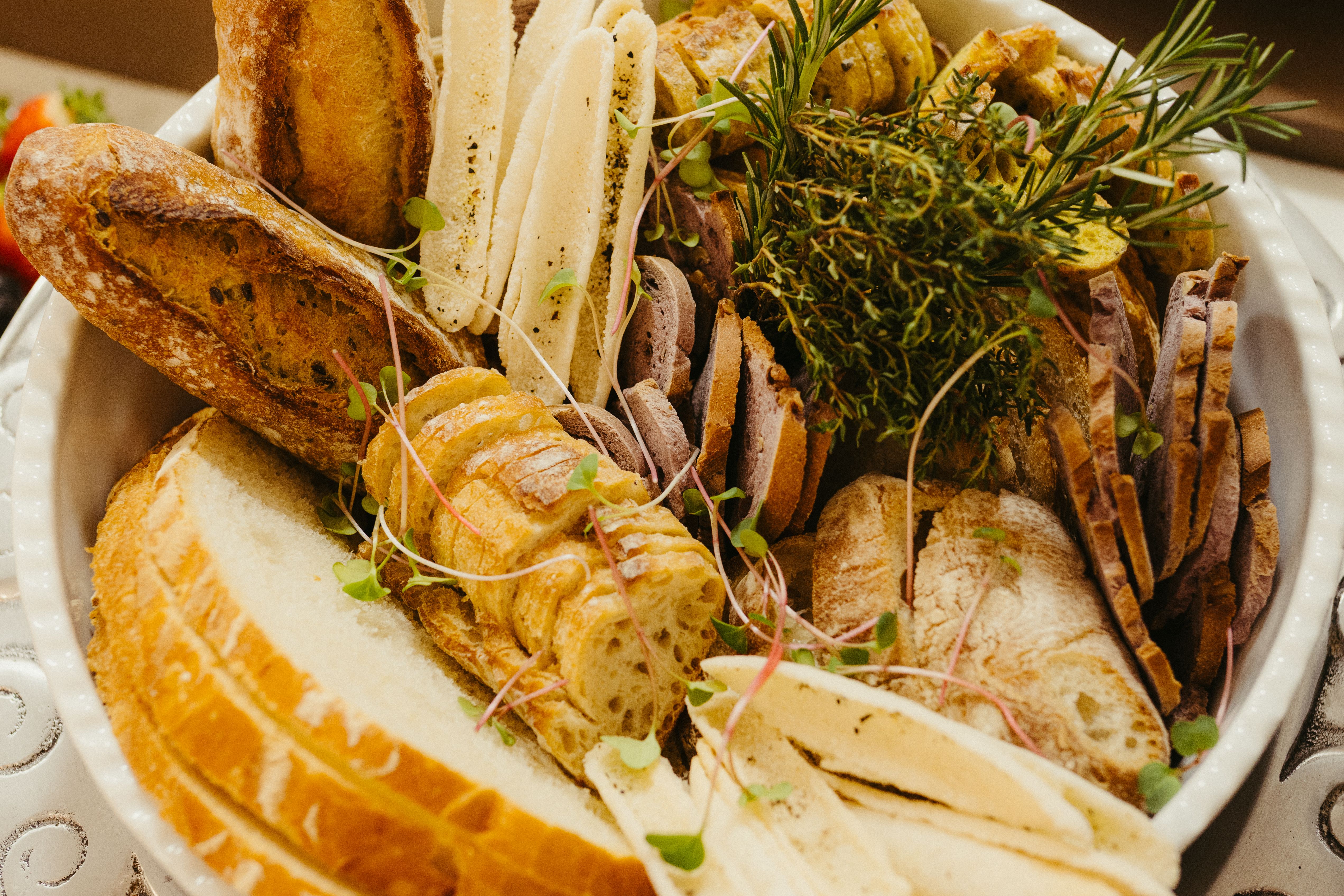 A selection of artisan breads displayed with fresh herbs in a decorative bowl, perfect for entertaining.