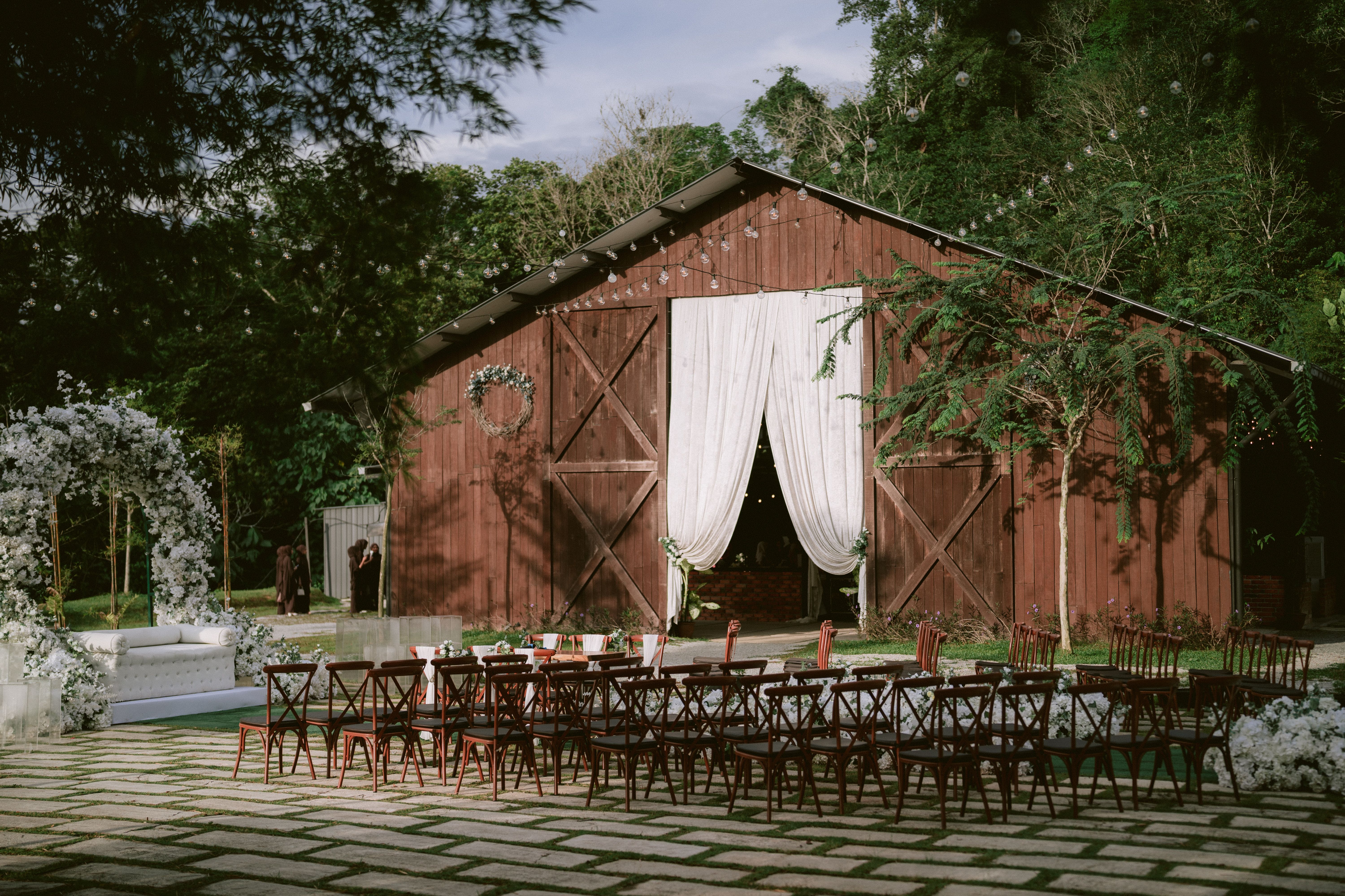 Outdoor rustic barn wedding setup with chairs and floral decorations in a scenic garden setting.