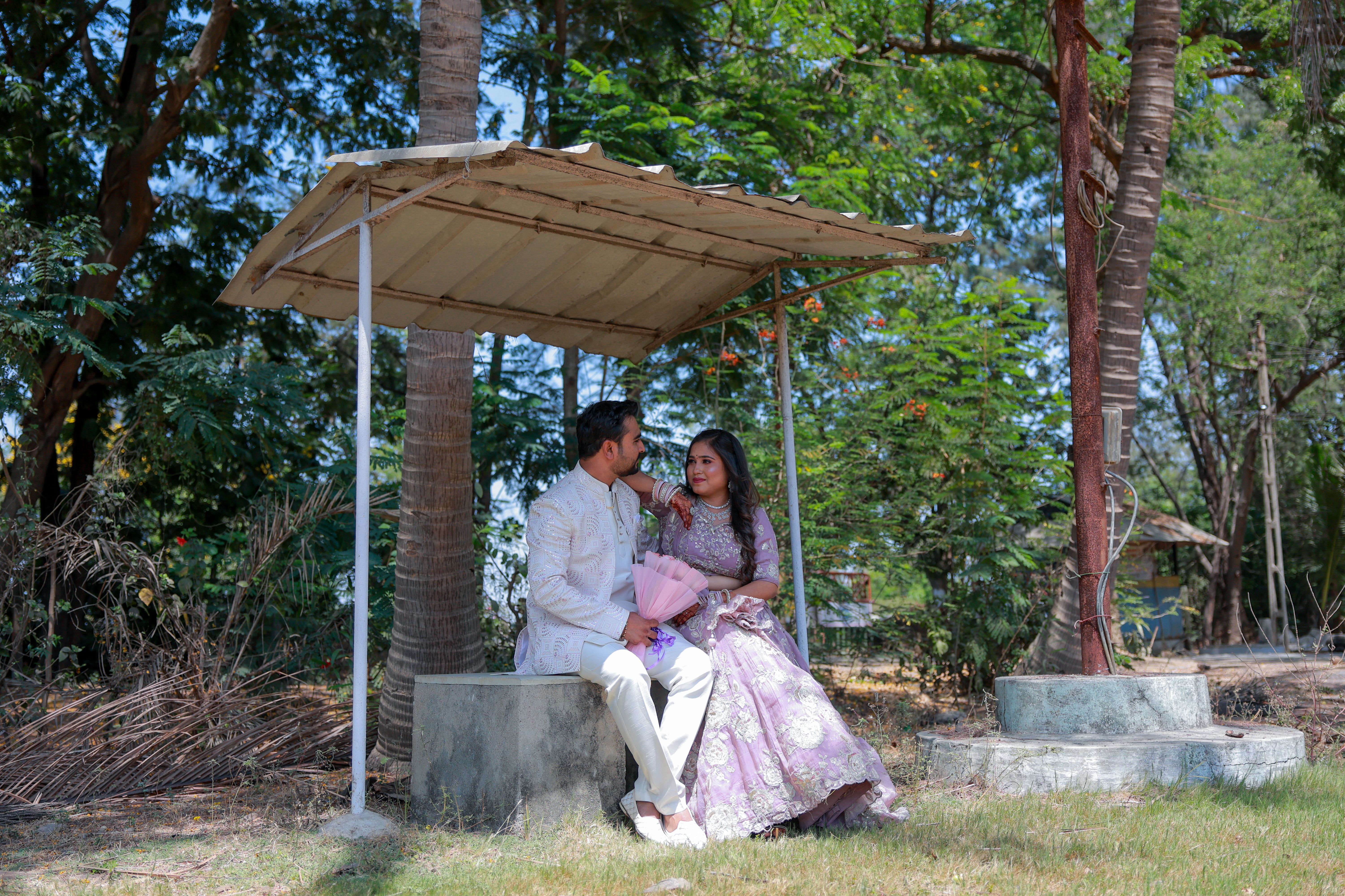 A bride and groom share a moment of love under a rustic shelter surrounded by lush greenery.