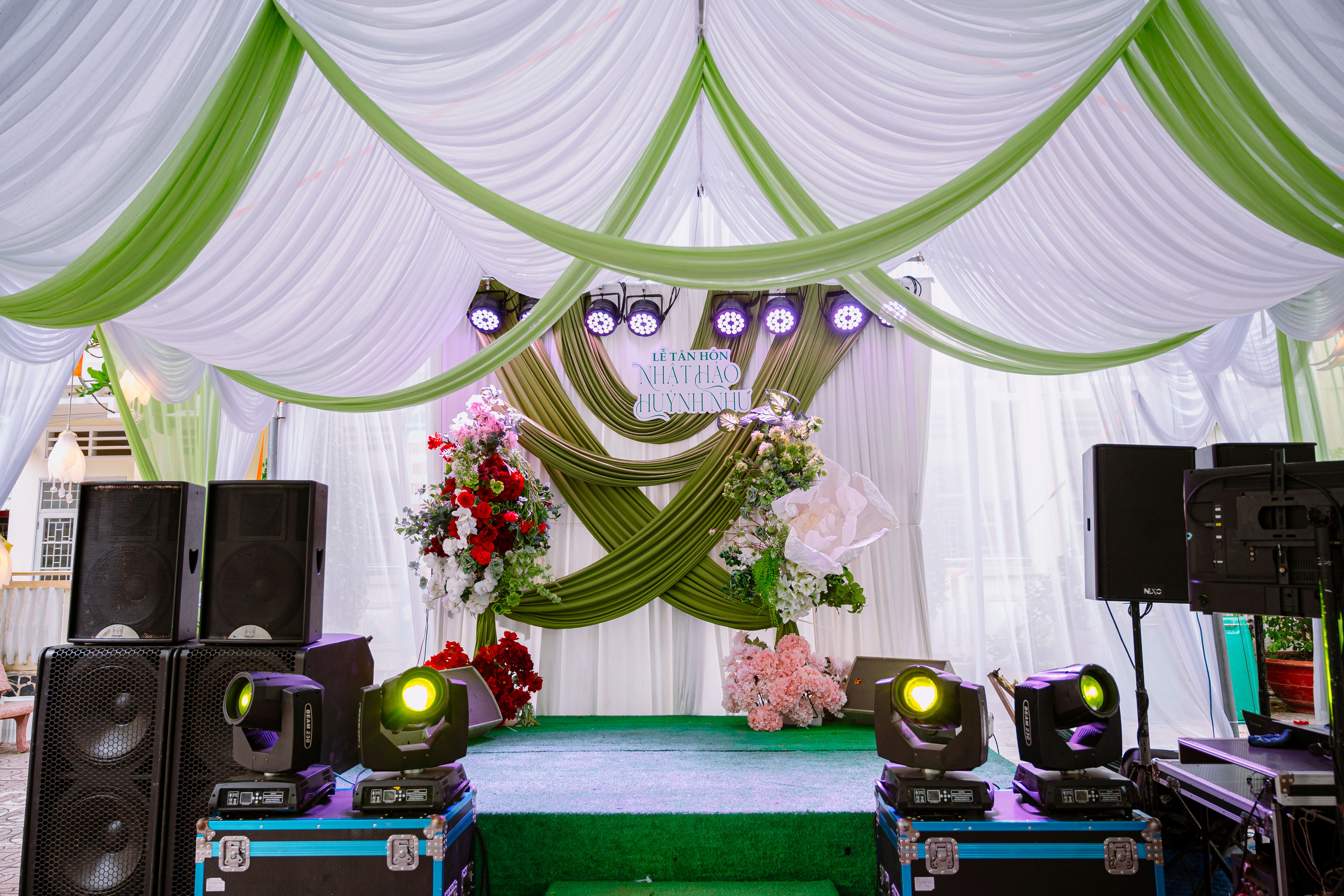 Beautifully decorated wedding stage with green and white drapes and floral arrangements.